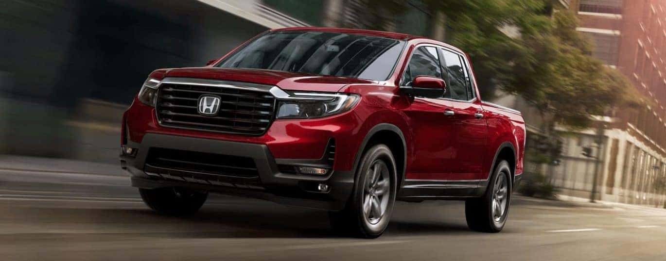 A red 2022 Honda Ridgeline RTL-E is shown driving on a city street.