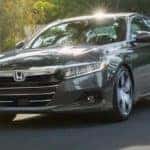 A grey 2021 Honda Accord Hybrid Touring is shown from the front at an angle while driving.