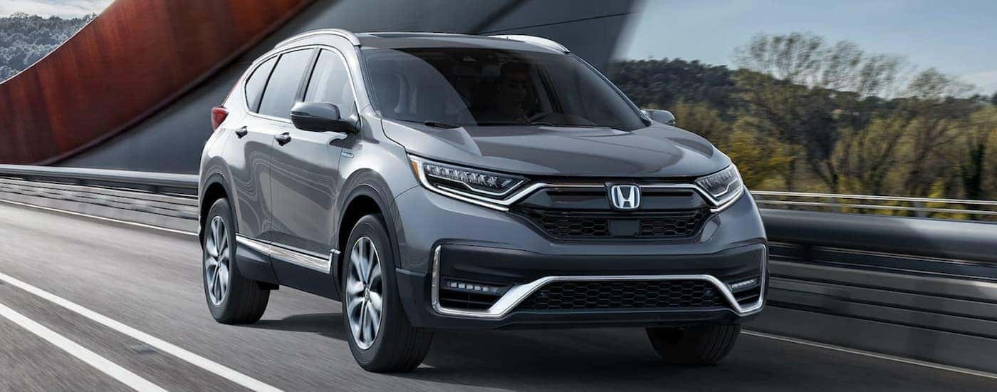 A grey 2022 Honda CR-V Hybrid Touring is shown driving on an open road.