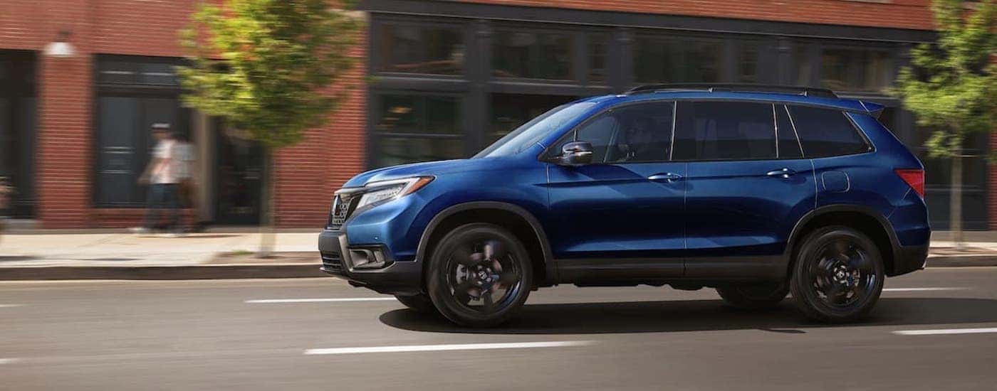 A blue 2021 Honda Passport is shown from the side while driving on a city street.