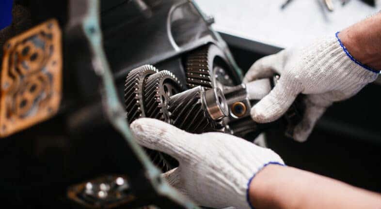 Close-up of a mechanic taking apart a car's transmission.
