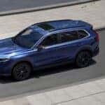 Blue 2025 Honda CR-V Sport Touring Hybrid driving on a city street.