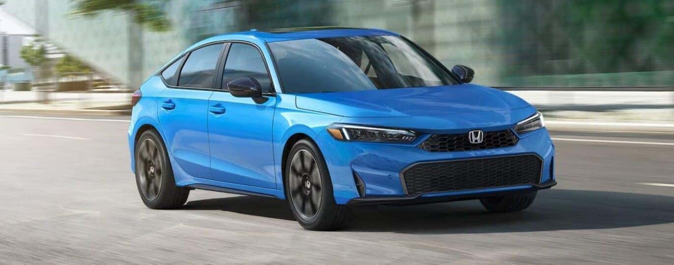 A blue 2025 Honda Civic Hatchback Sport Touring is shown driving on a city street.