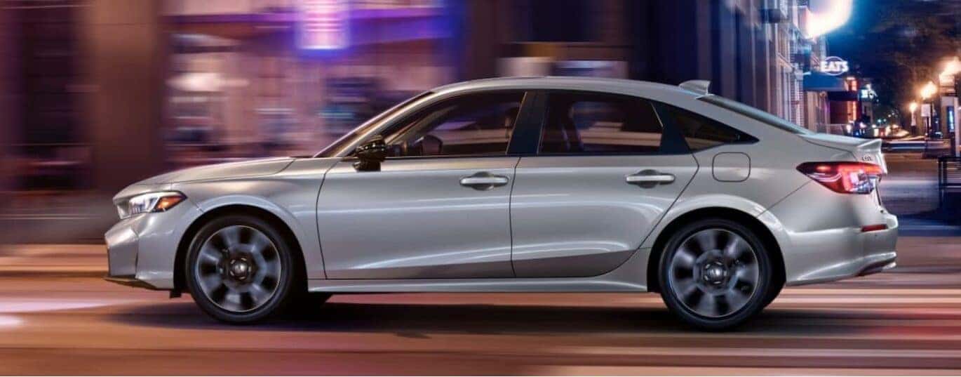 A silver 2025 Honda Civic Hybrid is shown driving fast on a city street.