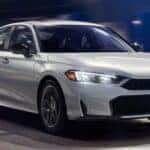 A white 2025 Honda Civic Sport Hybrid is shown driving at night.