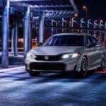 A silver 2025 Honda Civic for sale in Rochester is shown driving at night.