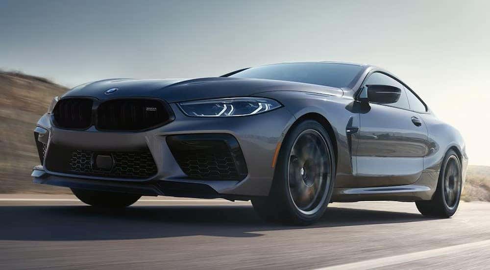 A gray 2024 BMW M8 Coupe is shown driving on a highway.