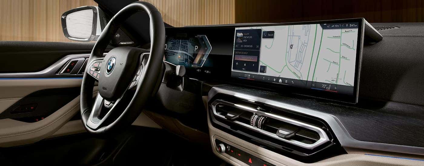 The steering wheel and curved infotainment display in a 2024 BMW i4 for sale.