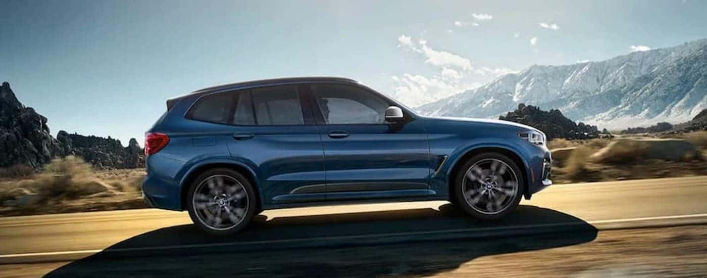 A blue 2020 BMW X3 is shown driving uphill on a highway.