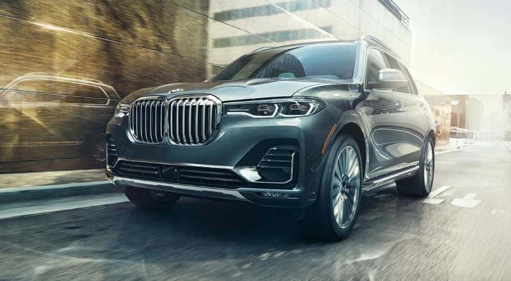 A popular used BMW for sale, a grey 2022 BMW X7, is shown driving on a city street.