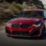 A popular BMW for sale near Dallas, a red 2025 BMW 2 Series, is shown on an open road.