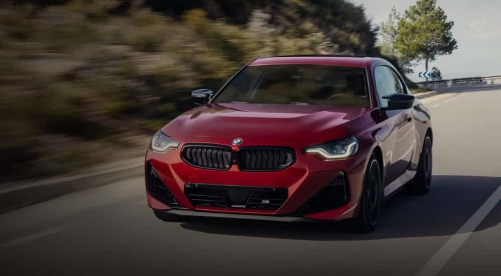 A popular BMW for sale near Dallas, a red 2025 BMW 2 Series, is shown on an open road.