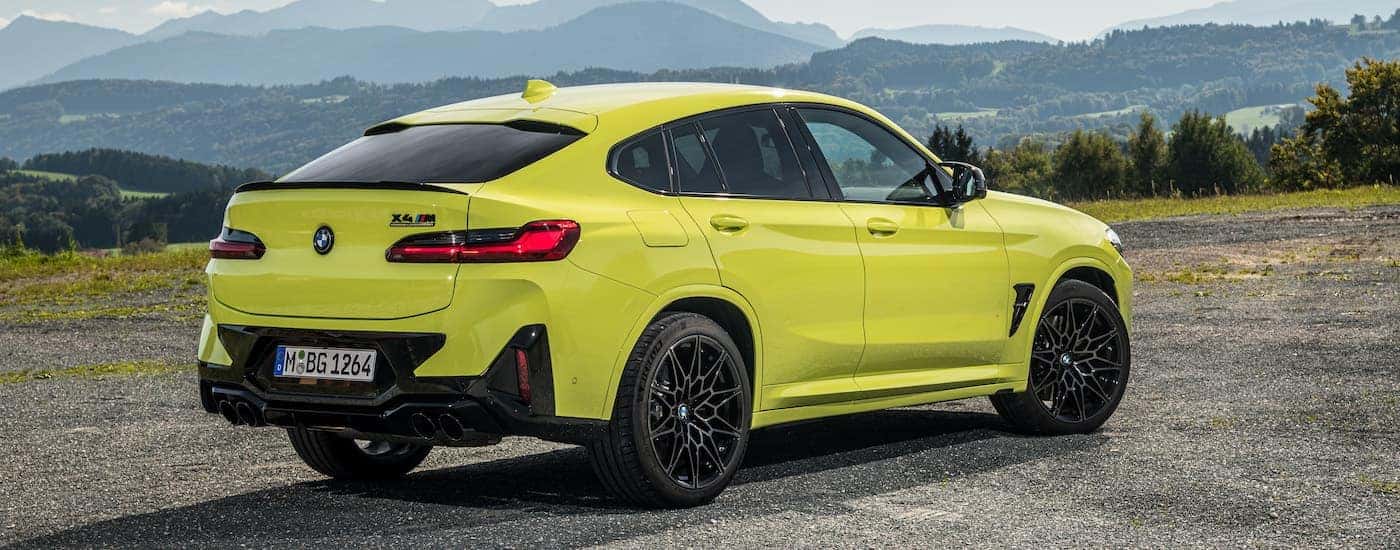 A yellow 2024 BMW X4M is shown from the rear at an angle.