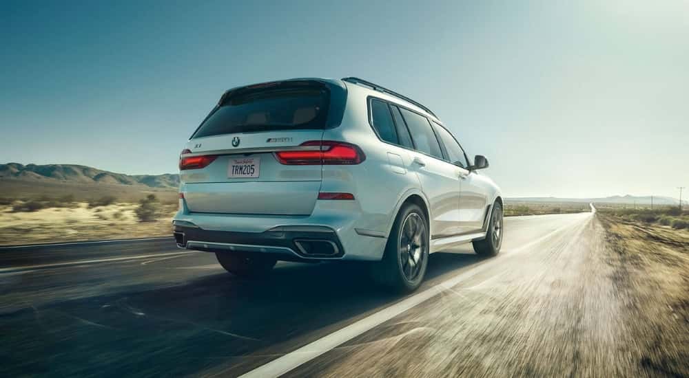 A white 2022 BMW X7 is shown from the rear driving on an open road.