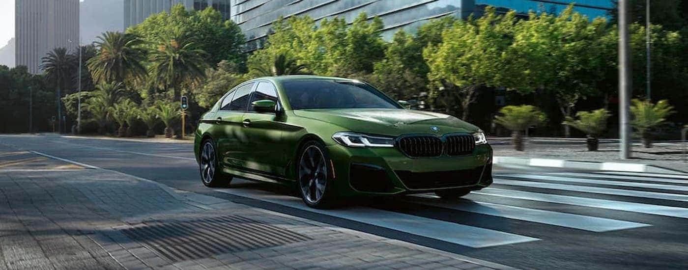 A green 2022 BMW M550i leaving a dealer that has a Certified Pre-Owned BMW.