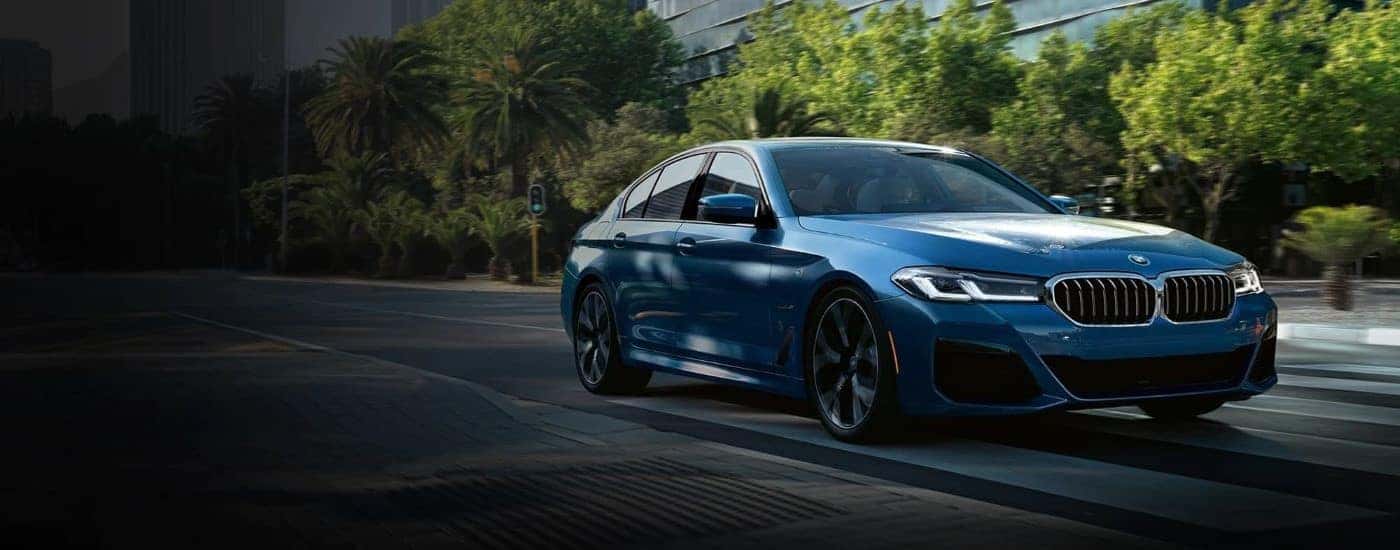 A blue 2023 BMW 530e is shown driving to view a used BMW for sale.