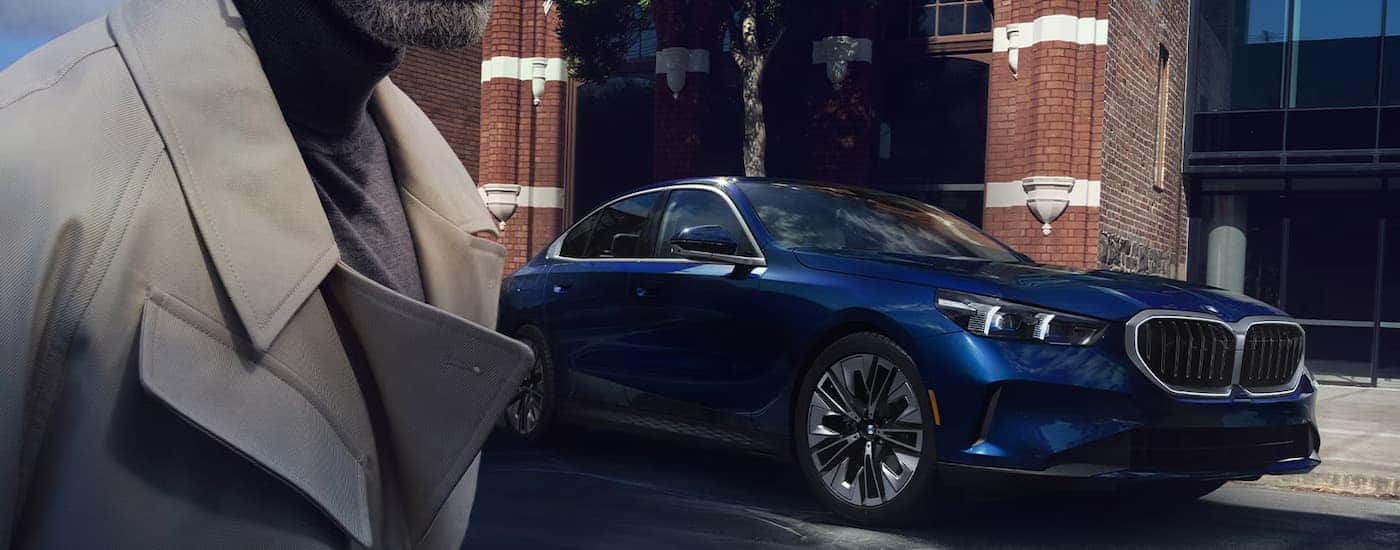 A blue 2024 BMW 5 Series sedan parked on the side of a city street.