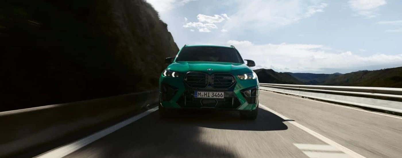 A green 2024 BMW X5 M driving toward the camera on an open road.