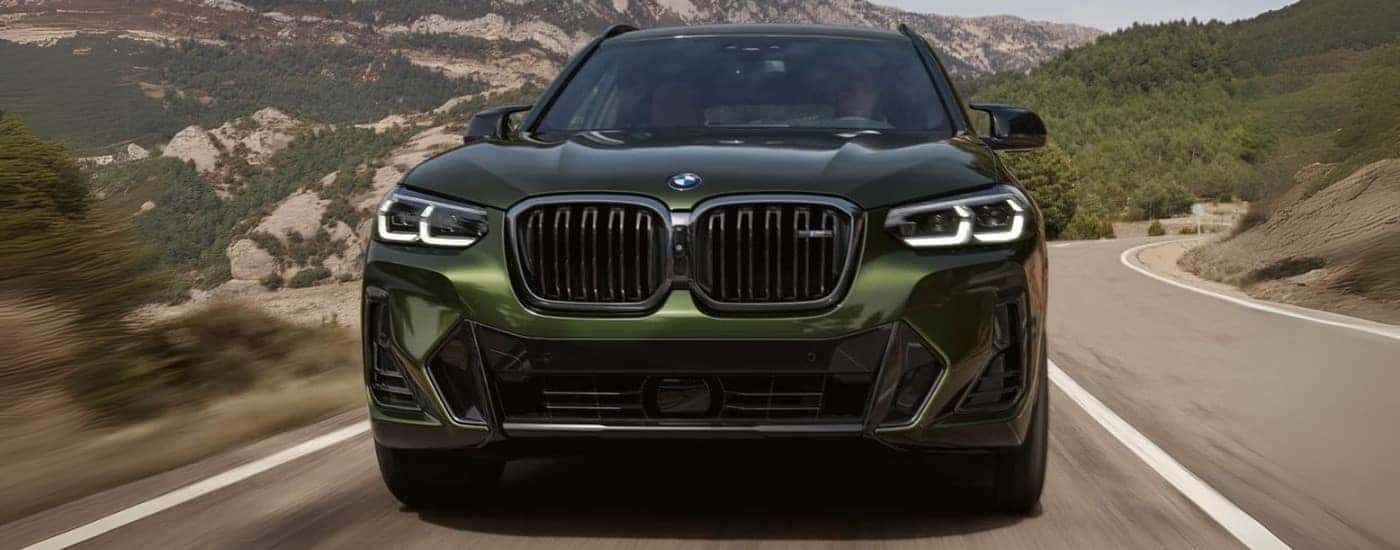 Green 2024 BMW X3 M50 driving down a road.