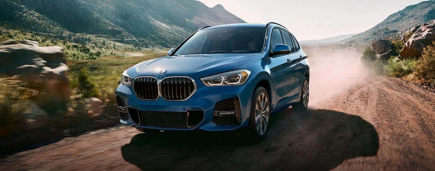 A blue 2022 BMW X1 M Sport driving on a dusty trail.