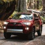 A red 2021 Toyota 4Runner is driving on a dirt road in the woods.