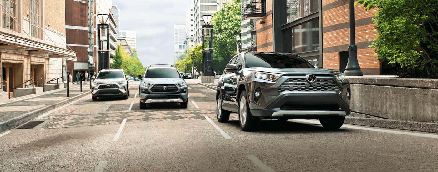 Three Toyota SUVs, all 2021 Toyota RAV4s, are driving on a city road across three lanes.