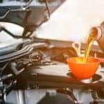 A mechanic is pouring oil into a funnel over a motor.