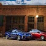 A blue and a red 2021 Toyota Mirai are parked in front of a brick building angled right.