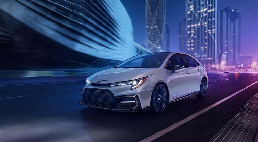 A white 2021 Toyota Corolla Hybrid is driving on a city street at night.