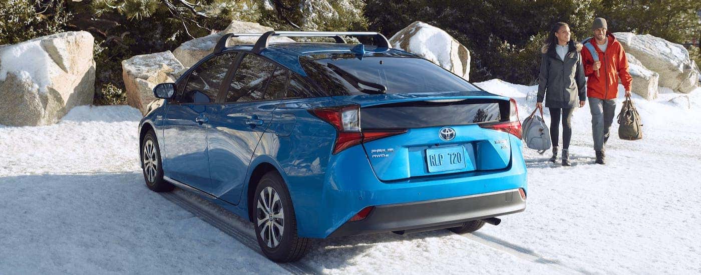 The forefather of the Toyota Hybrids, a blue 2021 Toyota Prius, is parked on snow with a couple walking towards it.