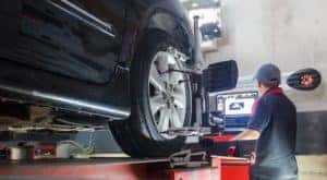 A mechanic is performing a Wheel Alignment on a black car that is on a lift.