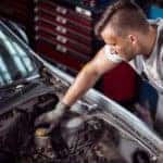 A mechanic is shown removing the brake fluid reservoir cap on a vehicle
