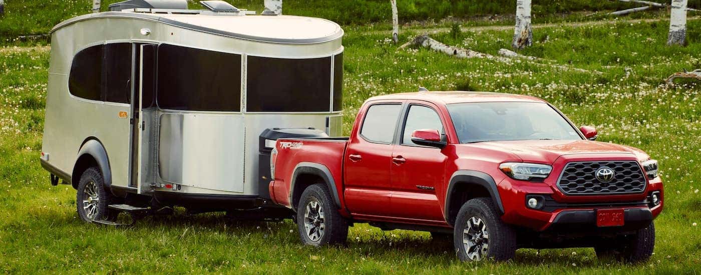 A red 2021 Toyota Tacoma from a Toyota truck dealer is parked on grass with a silver camper.