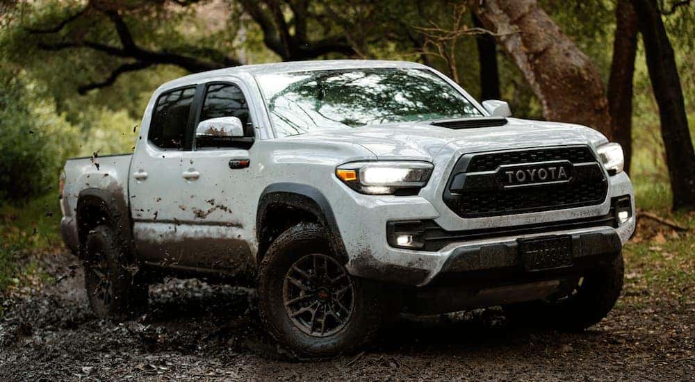 A white 2021 Toyota Tacoma is off-roading in the mud.