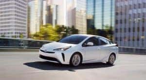 A white 2019 Toyota Prius from a used Toyota dealer is driving past a city.