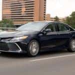 A black 2021 Toyota Camry is driving on a city street after getting a great Toyota lease deal.