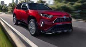 A red 2021 Toyota RAV4 Prime is driving on a two-lane road away from a city.