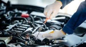 A close up shows gloved hands checking the oil level on an orange dipstick.
