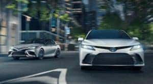 A silver and a white 2021 Toyota Camry are driving on a city street at night.