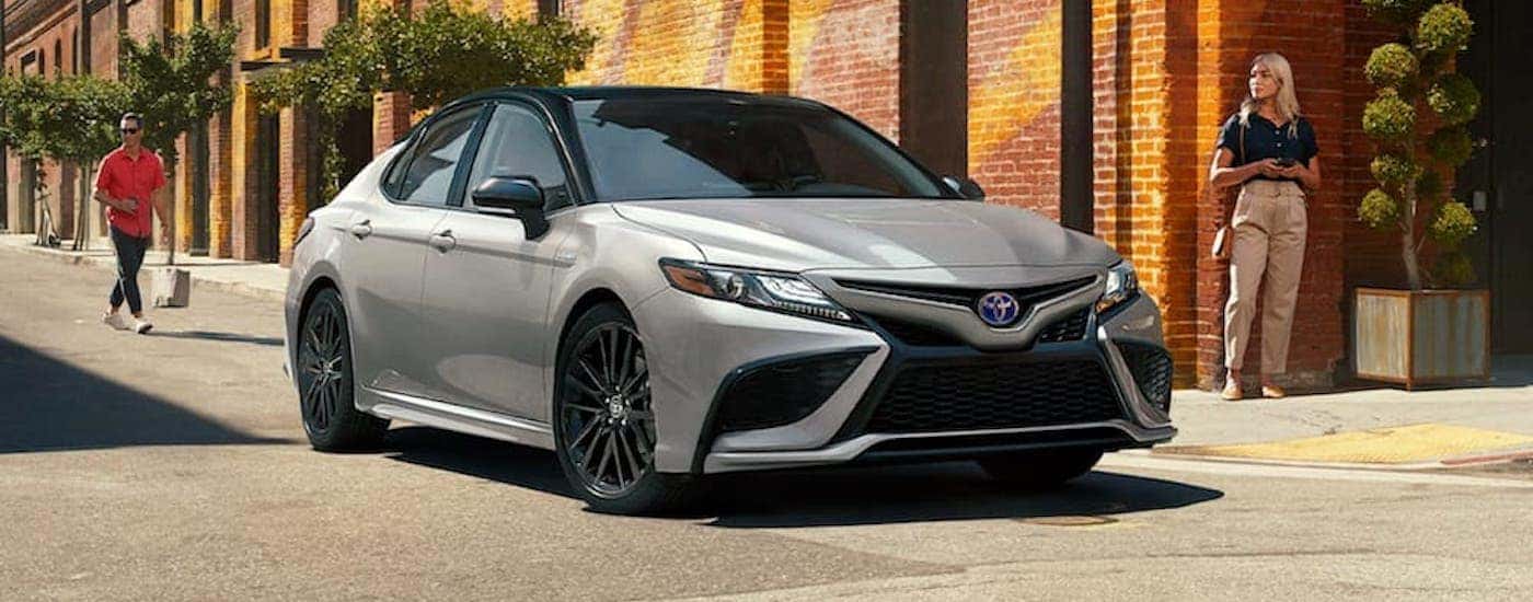 A silver and black 2021 Toyota Camry Hybrid is on a city street after leaving a Toyota Camry dealer.