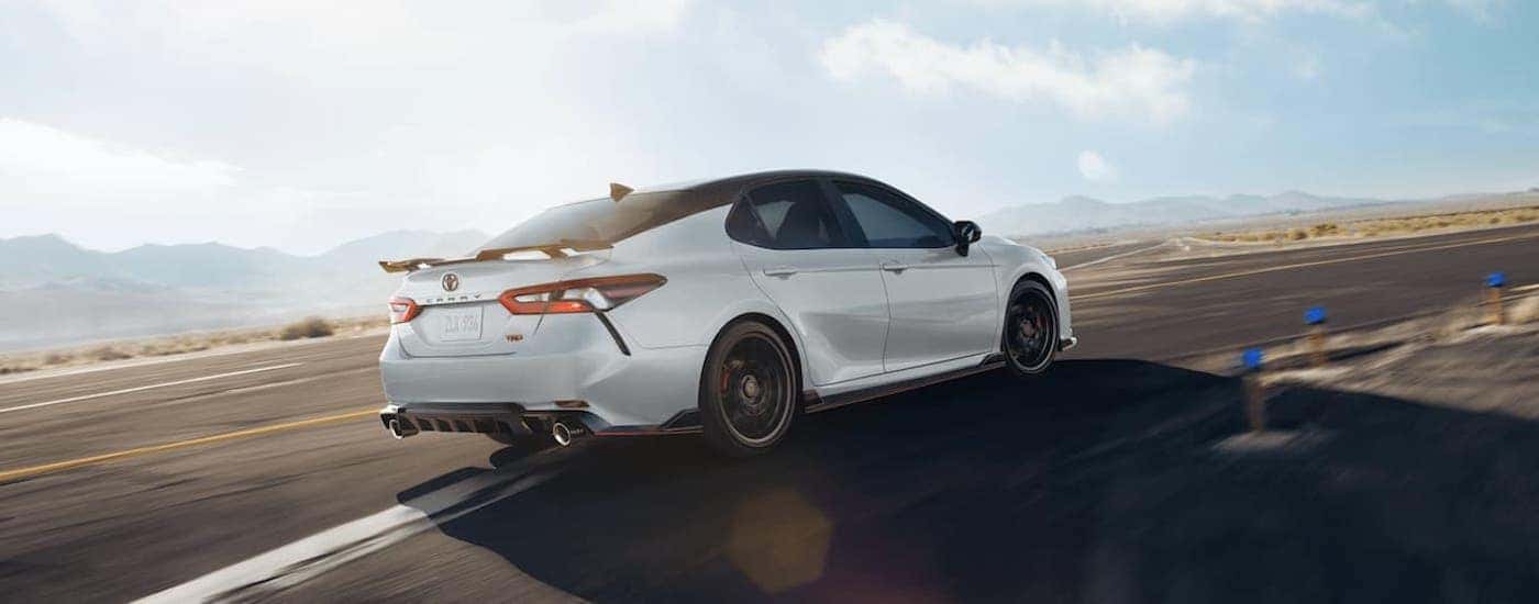 A white 2021 Toyota Camry is racing around a corner past desert mountains.