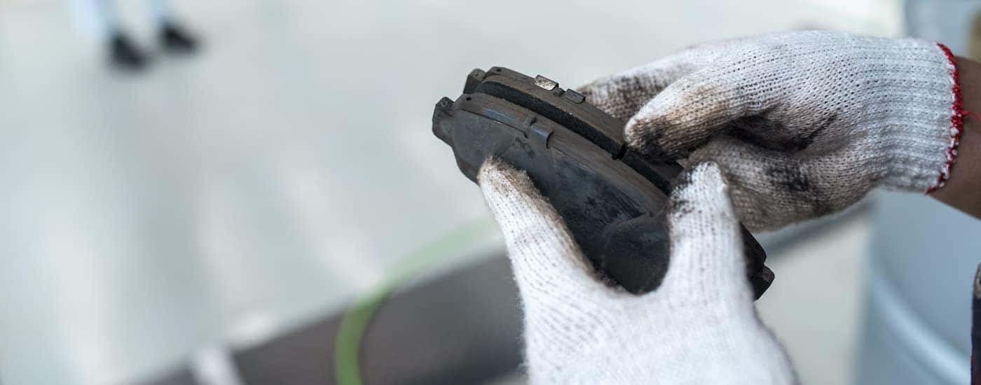 A close up shows gloved hands holding a set of brake pads.