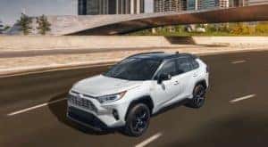 A white 2021 Toyota RAV4 is driving past a bridge after leaving a Toyota RAV4 dealer.