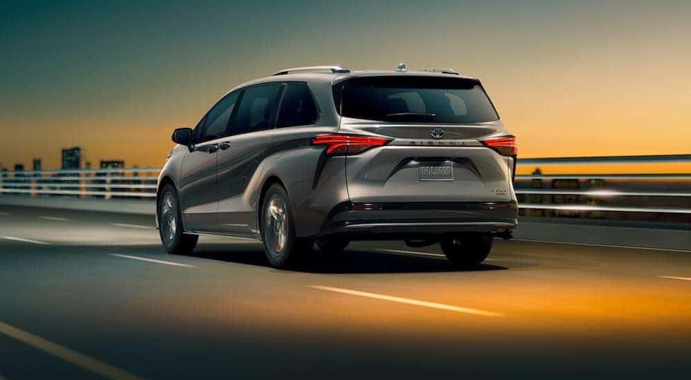 A grey 2021 Toyota Sienna is driving past a city after receiving a Toyota Sienna service.