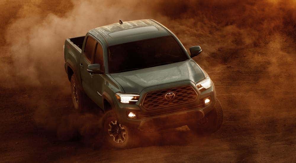 A green 2021 Toyota Tacoma is off-roading in the desert as sand gets kicked up.