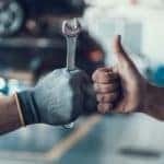A gloved hand holding a wrench is next to a hand giving a thumbs up at an affordable auto service center.