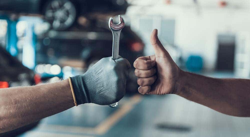 A gloved hand holding a wrench is next to a hand giving a thumbs up at an affordable auto service center.