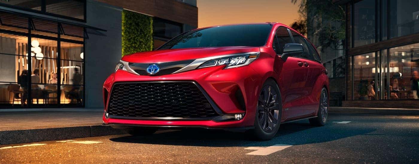 A red 2021 Toyota Sienna is shown from the side parked in front of shops.