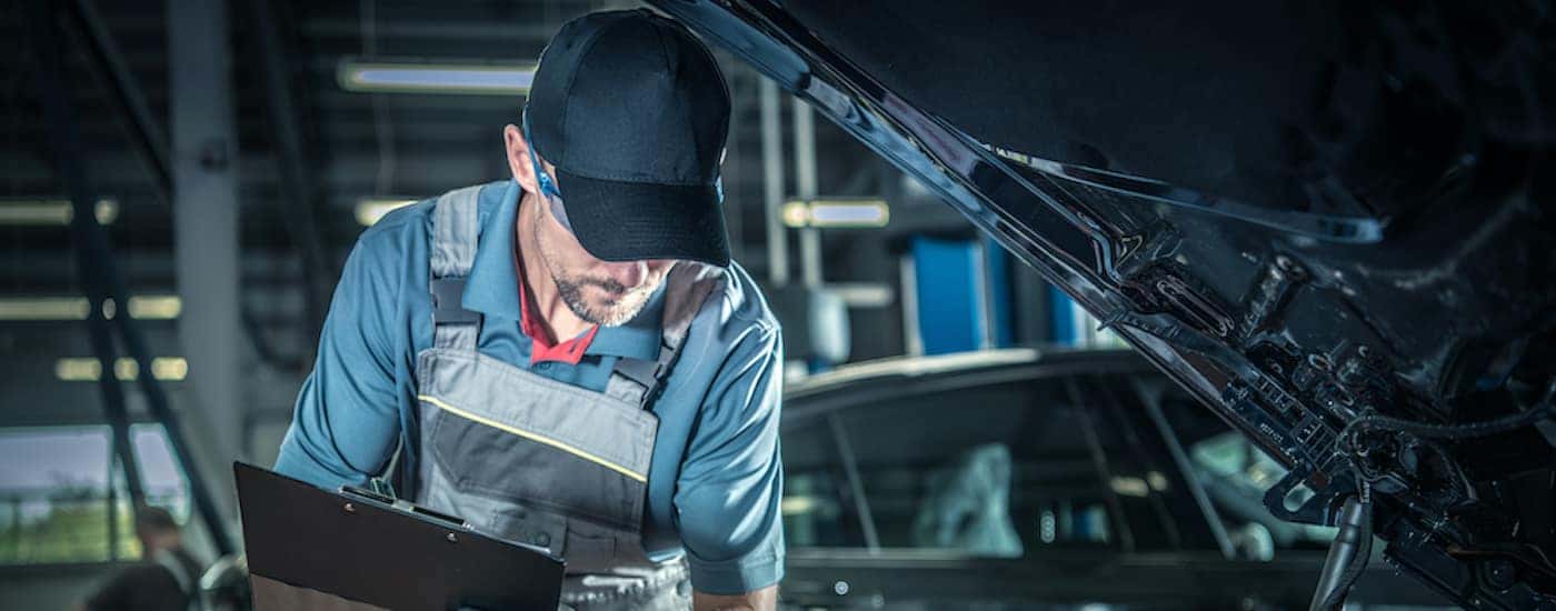 A mechanic is shown looking at an engine under the hood of a vehicle.