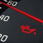 A close up of a car dashboard shows the check engine oil light.
